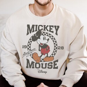A person wearing a white sweatshirt with a graphic of Mickey Mouse and text that says " Mickey Mouse".