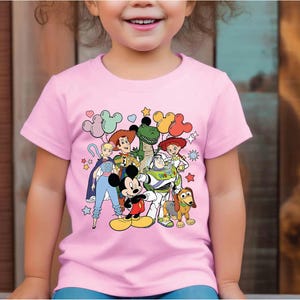 a little girl wearing a pink shirt with cartoon characters on it