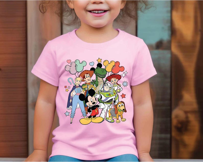 a little girl wearing a pink shirt with cartoon characters on it