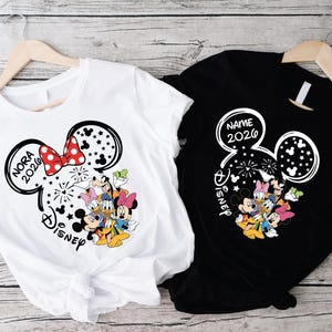 two t-shirts hanging on wooden hangers, each featuring a Disney character design.