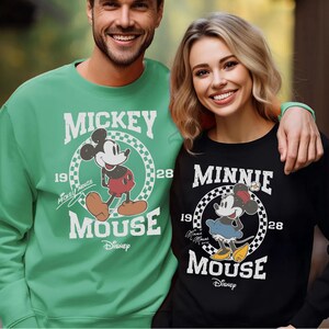 A man and a woman are standing together, both wearing Mickey Mouse sweatshirts.