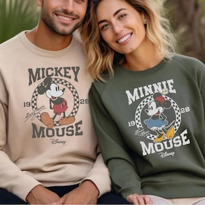 A man and a woman are sitting next to each other, both wearing Mickey Mouse sweatshirts.