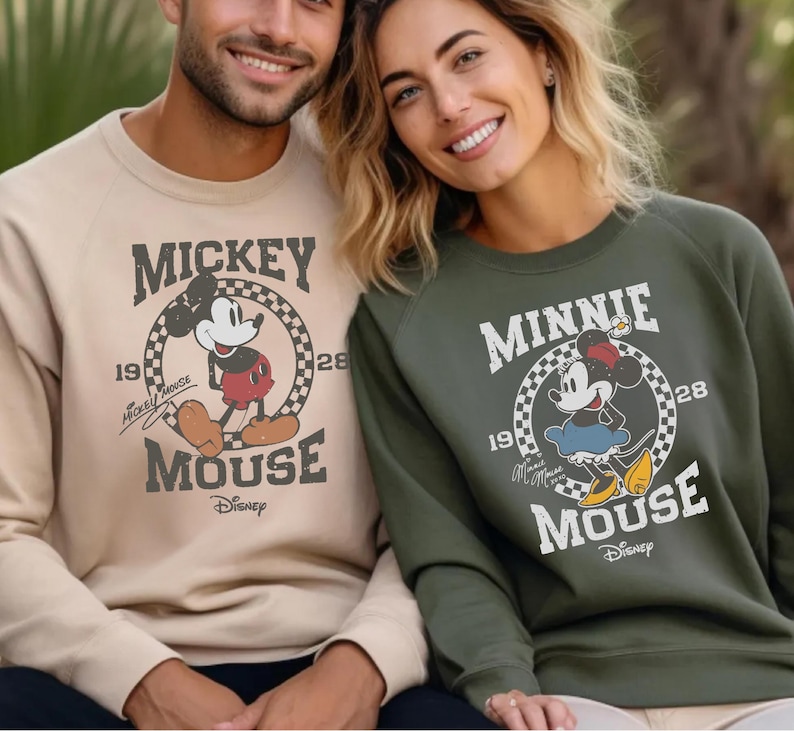 A man and a woman are sitting next to each other, both wearing Mickey Mouse sweatshirts.