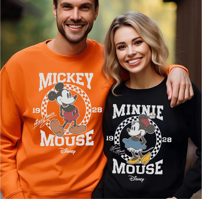 A man and a woman are standing together, both wearing Mickey Mouse sweatshirts.