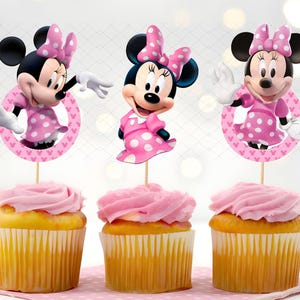 May include: Three cupcakes with pink frosting and Minnie Mouse toppers. Each cupcake has a yellow base and a pink swirl of frosting. The Minnie Mouse toppers feature the character in a pink dress with white polka dots.
