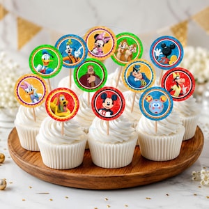 May include: A collection of round cupcake toppers featuring colorful illustrations of various cartoon characters, including Mickey Mouse, Minnie Mouse, Donald Duck, and Pluto, each mounted on a small wooden pick and inserted into white frosted cupcakes.