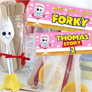 Può includere: Una forchetta di plastica bianca con un volto disegnato e braccia in scovolini rossi, in stile del personaggio Forky. L'immagine include banner rosa con il testo "Make Your Own Forky" e "Thomas Story 2", insieme a materiali per l'artigianato.