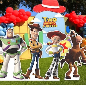 May include: A decorative party backdrop featuring cardboard cutouts of Buzz Lightyear, Woody, Jessie, and Bullseye from Toy Story. The display includes a red cowboy hat, red and blue balloon arches, and text reading Two Infinity & Beyond.