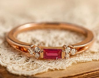 May include: Rose gold ring featuring a rectangular ruby gemstone and small diamond accents. The ring is set on a vintage book with a lace doily. The ring is a piece of jewelry.