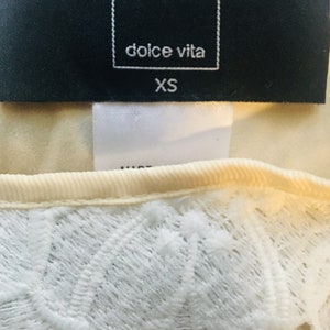 May include: A white lace top with a black tag that says "dolce vita" and "XS".