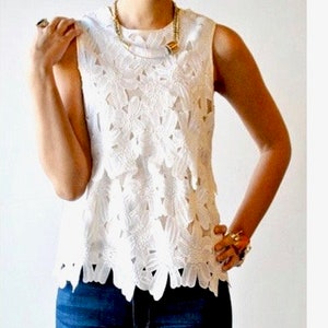 May include: White sleeveless lace top with a floral pattern. The top has a scalloped hem and is made of a delicate fabric.