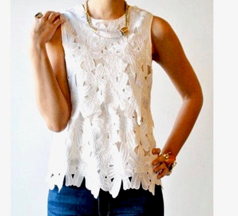 May include: White sleeveless lace top with a floral pattern. The top has a scalloped hem and is made of a delicate fabric.