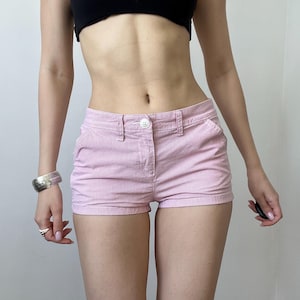 May include: Pink and white striped shorts with a button closure and pockets. The shorts are made of a lightweight fabric and have a classic, casual style. The shorts are a light pink color with thin white stripes.