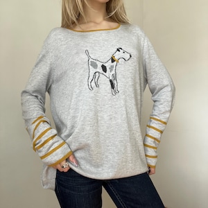 Könnte beinhalten: Hellgrauer Pullover mit Hundegrafik. Der langärmlige Pullover hat senffarbene Abschlüsse an Ausschnitt und Ärmeln. Die Hunde-Grafik ist schwarz, weiß und grau mit gelbem Halsband.