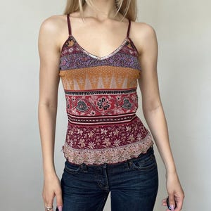 Könnte beinhalten: Ein ärmelloses Camisole-Top mit V-Ausschnitt, dünnen weinroten Trägern und silbernem Paillettenbesatz. Das Kleidungsstück zeigt ein mehrfarbiges horizontales Muster mit Blumen- und Paisley-Motiven in den Farben Weinrot, Orange, Lila und Creme.