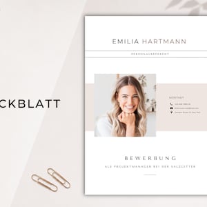 May include: A resume template with the name "Emilia Hartmann" at the top. The document includes a photo of a smiling woman, contact information, and the word "Deckblatt" and "Bewerbung" in the design. Two gold paper clips are at the bottom.