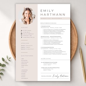 Könnte beinhalten: Eine professionelle Lebenslaufvorlage mit einem Foto einer lächelnden Frau mit dem Titel "Emily Hartmann, Marketing Managerin". Der Lebenslauf enthält Abschnitte für Kontaktinformationen, Sprachen, Qualifikationen und Fähigkeiten. Ein goldener Stift und ein kleiner goldener Stifthalter liegen auf dem Holztablett.