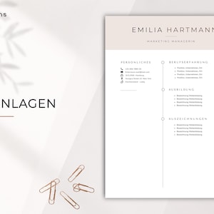 May include: A resume template with a light beige and white color scheme. The name "Emilia Hartmann" and the title "Marketing Managerin" are at the top. The word "ANLAGEN" is in the lower left corner. Several gold paper clips are scattered.