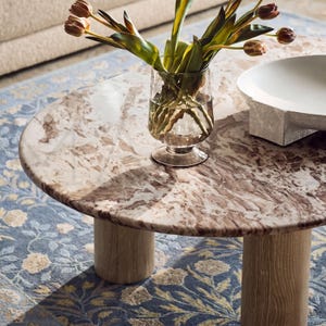 A marble-topped coffee table with a vase of tulips and a white bowl on it, placed on a blue and white patterned rug.