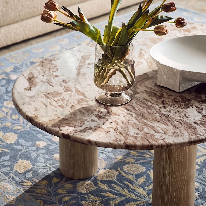 A marble-topped coffee table with a vase of tulips and a white bowl on it, placed on a blue and white patterned rug.