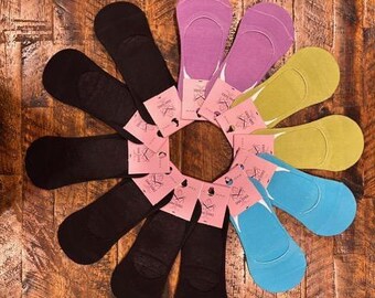 May include: An overhead shot of a collection of no-show socks in various colors, including black, purple, yellow, and blue. Each pair of socks has a small tag attached. The socks are arranged in a circular pattern on a wooden surface.