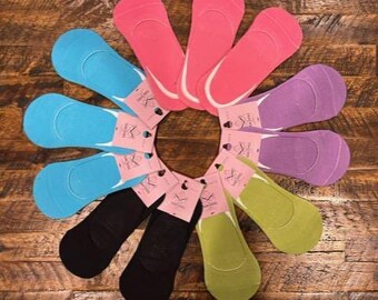Puede incluir: Una colección de calcetines invisibles de colores, dispuestos en forma circular. Los calcetines vienen en varios colores, incluyendo rosa, azul, negro, verde y morado. Cada par tiene una etiqueta. Los calcetines se exhiben sobre una superficie de madera.