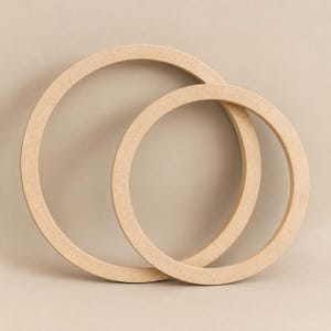 May include: Two circular rings made of light brown, unfinished wood material. The rings are of different sizes, with the smaller ring partially overlapping the larger ring, creating a simple, geometric composition with a flat, matte texture.