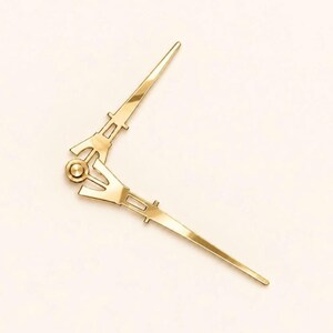 May include: A pair of gold-colored clock hands featuring a metallic finish and a pointed design. The two hands are connected at a central circular hub, with one hand extending upward and the other extending downward at an angle.