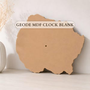 Può includere: Un quadrante per orologio in MDF color marrone chiaro a forma di geode, con contorno organico irregolare e superficie piatta e liscia. Un piccolo foro circolare centrale è visibile per l'installazione del meccanismo. Testo GEODE MDF CLOCK BLANK.