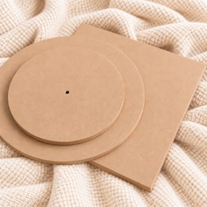 May include: A set of three light brown, smooth, flat wooden shapes consisting of two circular discs and one rectangular board. The smaller circular disc features a single, centered, small circular hole, while the larger disc and the rectangle are solid.