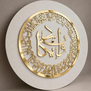 May include: A circular wall clock featuring a matte off-white base and a metallic gold finish. The clock face displays intricate Arabic calligraphy in a cut-out style, with a central focal point and a border of script surrounding the perimeter.