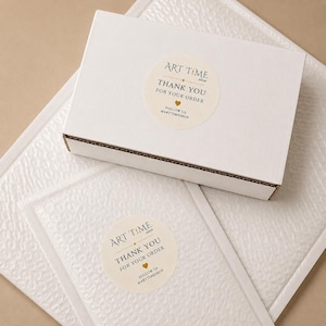 May include: A white rectangular cardboard shipping box and a white bubble mailer, each featuring a round cream-colored sticker. The stickers display the text ART TIME SHOP, THANK YOU FOR YOUR ORDER, a small gold heart, and FOLLOW US @ARTTIMESHOP.