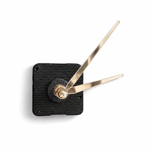 May include: A black square clock movement mechanism featuring a textured surface and a central gold-colored nut. Two slender, metallic gold clock hands are attached to the center, extending outward at an angle to indicate time.
