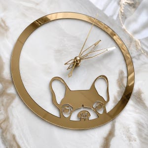 May include: A circular wall clock with a reflective gold finish. The frame features a cutout silhouette of a French Bulldog head at the bottom. The clock has thin, gold-colored hour, minute, and second hands centered within the open circular frame.