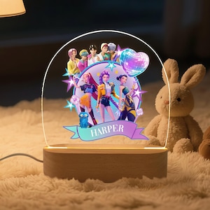 May include: A decorative LED lamp featuring a colorful illustration of a group of people, a disco ball heart, and the name "HARPER" on a banner. The lamp has a wooden base and a clear acrylic panel.