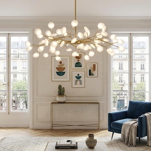 Könnte beinhalten: Ein modernes Wohnzimmer mit einem goldenen Kronleuchter, abstrakter Kunst und einem blauen Sessel. Der Raum verfügt über große Fenster, einen Konsolentisch und einen gemusterten Teppich. Der Kronleuchter hat mehrere kugelförmige Lichter.