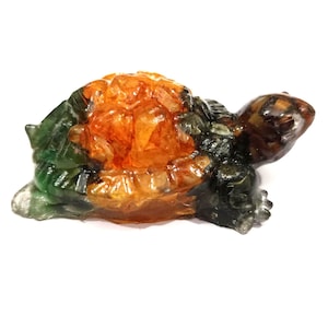 May include: A small turtle figurine carved from translucent stone, featuring a vibrant orange shell with a faceted texture, contrasted by deep green and dark brown tones on the head, limbs, and tail, creating a multi-colored, polished appearance.