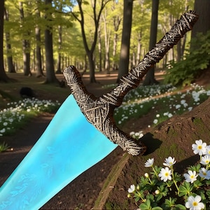 Könnte beinhalten: Ein Fantasy-Schwert mit einem geflochtenen braunen Griff und einer leuchtenden blauen Klinge. Die Klinge hat ein eingraviertes Blumendesign. Das Schwert liegt auf einem Baumstamm in einem Wald, mit weißen Blumen im Vordergrund.