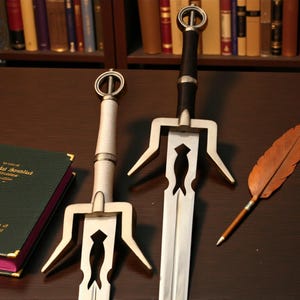 Può includere: Due spade decorative con lame argentate e manici ornati, una nera e una bianca. Una penna di piuma di cuoio e un libro verde con scritte dorate sono anche sulla superficie marrone scuro. Lo sfondo presenta una libreria piena di libri.