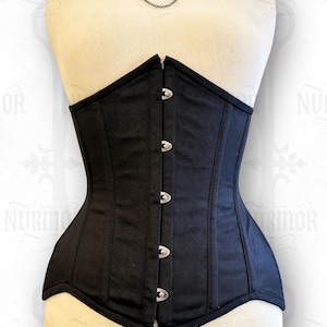May include: A black corset with a structured silhouette, featuring a front closure with silver-toned clasps. The corset is displayed on a mannequin, showcasing its form-fitting design. The garment has a classic, elegant aesthetic.