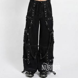 Peut inclure: Pantalon cargo en jean noir avec une taille haute et un cordon de serrage. Le pantalon présente de multiples sangles, des œillets métalliques argentés, des anneaux en D et des poches cargo latérales. Les jambes ont des sangles réglables.