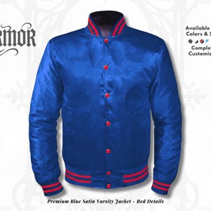 Op de afbeelding: Een blauwe satijnen varsity jack met rode accenten op de kraag, manchetten en zoom. De jas heeft rode knopen en de tekst "NURMOR". De tekst "Available in All Colors & Sizes" is ook zichtbaar.