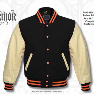 Op de afbeelding: Zwarte varsity jas met crèmekleurige leren mouwen. De jas heeft een zwarte wollen body, oranje en zwart gestreepte manchetten en tailleband, en oranje accenten op de kraag. De tekst "NURMOR" is zichtbaar. Verkrijgbaar in alle kleuren en maten, volledig aanpasbaar.