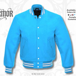 Op de afbeelding: Een hemelsblauw varsity jack met een opstaande kraag, lange mouwen en een knoopsluiting aan de voorzijde. De kraag, boorden en zoom zijn voorzien van witte strepen. De tekst NURMOR staat links, met Available in All Colors & Sizes.