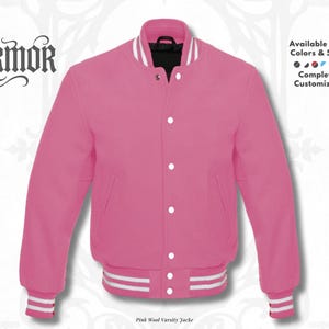 Pode incluir: Uma jaqueta varsity rosa brilhante com acabamento canelado listrado em branco na gola, punhos e bainha. A jaqueta possui fecho frontal com botões de pressão e dois bolsos laterais. O texto NURMOR aparece no lado esquerdo da imagem.