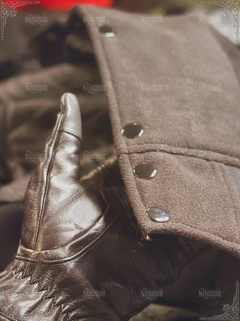 May include: Close-up of a brown leather glove with decorative stitching. The glove is next to a brown coat with three dark buttons. The coat has a textured, felt-like appearance.