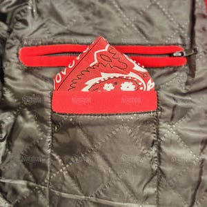 May include: Close-up of a quilted jacket interior. A red bandana with a white paisley design is tucked into a red-trimmed pocket. A red zippered pocket is visible above. The jacket's interior is a dark gray color.
