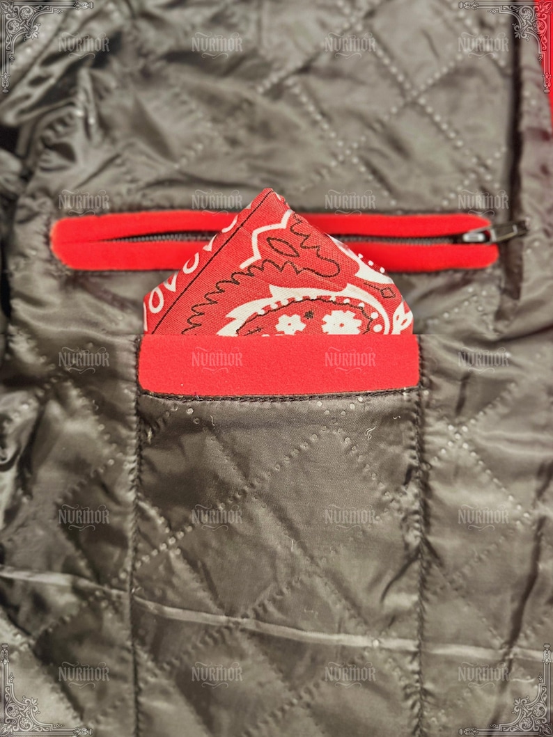 May include: Close-up of a quilted jacket interior. A red bandana with a white paisley design is tucked into a red-trimmed pocket. A red zippered pocket is visible above. The jacket's interior is a dark gray color.