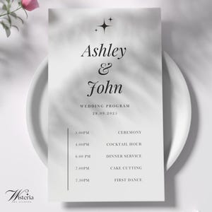 Puede incluir: Un programa de boda en un plato blanco. El programa presenta los nombres "Ashley & John" en una escritura elegante, con la fecha "28.09.2025" y un programa de eventos. El logotipo de Wisteria Art Studios está en la esquina inferior izquierda.