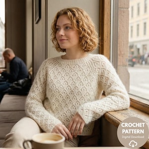 Puede incluir: Suéter de crochet color crema con un patrón de diamantes. El suéter tiene mangas largas y cuello redondo. La imagen también muestra una taza de café y un gráfico de descarga digital para un patrón de crochet.